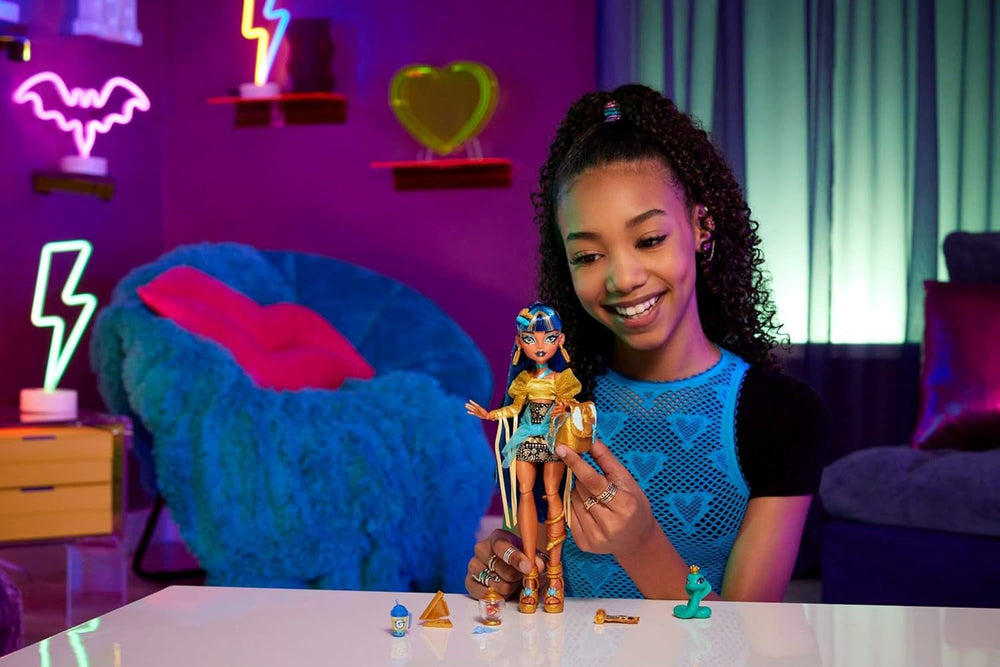 Păpușa Monster High Cleo De Nile într-o bluză aurie și o fustă cu mai multe straturi, include cobra Hissette și accesorii precum un ghiozdan, o gustare și un sul de hârtie igienică, HXH74